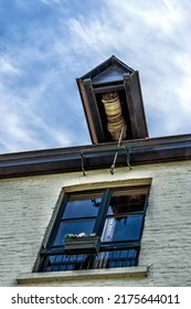 Closeup Of Slanted Pulley Hook And Beam At Gable On Top Of White Brick House Under Blue Sky.