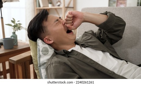 closeup of a sleepy asian guy lying on the sofa with a yawn while staying at home in the living room during quarantine. - Shutterstock ID 2240261261