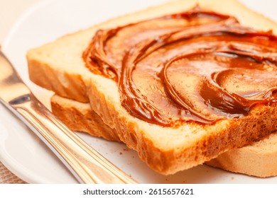 A close-up of a slice of bread with dulce de leche cream on top. Tilted view.