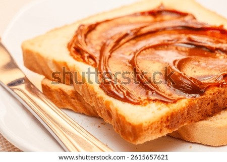 A close-up of a slice of bread with dulce de leche cream on top. Tilted view.