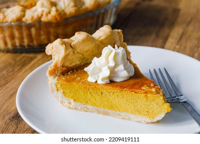 Close-up of a slice of Pumkin Pie on a white plate with fork, and a dollop of cream on the top.  - Shutterstock ID 2209419111