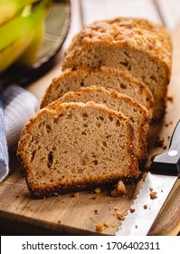 Closeup Of Sliced Banana Nut Loaf Cake On A Wooden Cutting Board With Bananas In Background