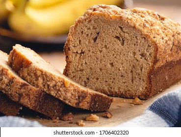 Closeup Of Sliced Banana Nut Loaf Cake On A Wooden Cutting Board With Bananas In Background