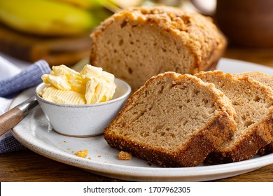 Closeup Of Sliced Banana Nut Loaf Cake And Butter On A Plate With A Bunch Of Bananas In Background