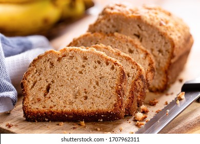 Closeup Of Sliced Banana Nut Loaf Cake On A Wooden Cutting Board With Bananas In Background