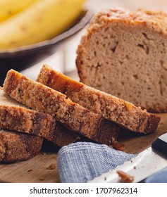 Closeup Of Sliced Banana Nut Loaf Cake On A Wooden Cutting Board With Bananas In Background