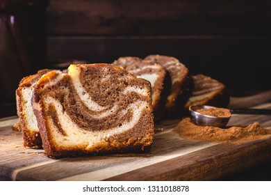 Closeup of sliced cinnamon swirl sweet bread and cinnamon spice on a wooden board in a dark rustic setting
