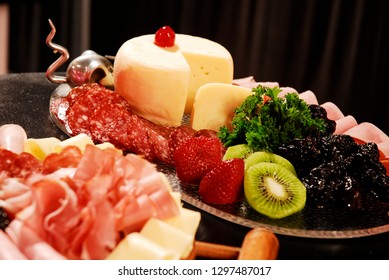 Closeup of sliced ham, salami, strawberries, kiwi fruit, plumb and cheese platters.