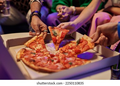 Close-up of slices of appetizing pizza in square cardboard box and hands of young friends taking them and eating while enjoying home party - Powered by Shutterstock