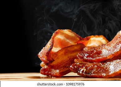 Closeup of slices of crispy hot freshly cooked bacon with copy space in black background