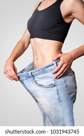 Close-up of slim waist of young woman in big jeans showing successful weight loss, isolated on light gray background, diet concept. - Shutterstock ID 1031943745