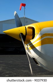 Close-Up Of Small Airplane Propeller With Out Of Focus Hanger And Windsock In The Background