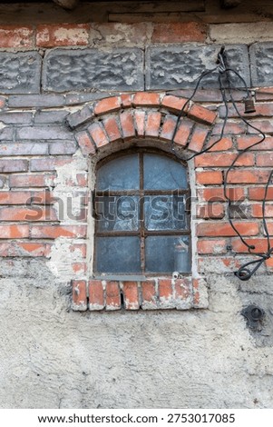 Close-up of small arched window on a weathered red brick wall of an old farm building, rustic architectural detail with vintage messy electrical wiring.