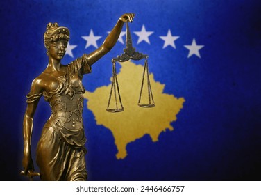 Close-up of a small bronze statuette of Lady Justice before a flag of Kosovo.
