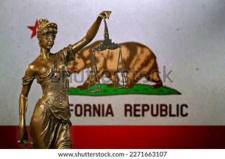 Close-up of a small bronze statuette of Lady Justice before a flag of California.