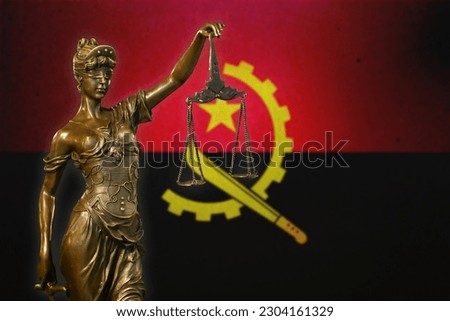 Close-up of a small bronze statuette of Lady Justice before an Angolan flag.