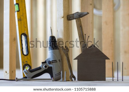 Close-up of small brown model house and building tools on wooden planks in unfinished room under construction background. Investments in real estate, property and ownership of dream home concept.