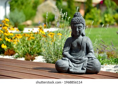 A closeup of a small Buddha statue in a garden with a blurry background