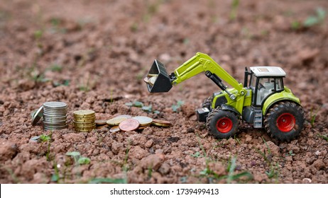 Closeup Of Small Green Agricultural Toy Tractor Loading Money Coins, Icon Farmer Machinery, Agriculture Business Concept