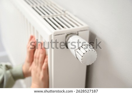 Close-up of small child’s hands warming on white home radiator. Winter heating, indoor comfort, safe temperature control, family energy use, cozy atmosphere and home warmth concept.