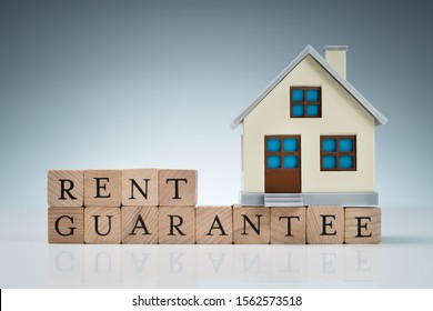 Close-up Of Small House Model On Wooden Blocks With Rent Guarantee Text Over Table