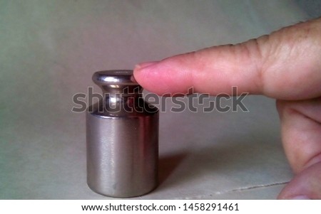 Close-up of a small metal weights for scales on which is pressed with the index finger. Light silver metal, part of the hand on a light background.
