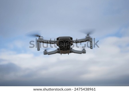 Closeup of small remotely controlled drone with camera hovering over a field, sky in the background