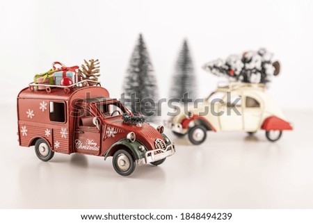 A closeup of small toy cars on the table with small Christmas trees in the background