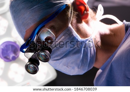 A closeup of a smart and confident surgeon performing an operation while looking through an advanced surgical loupe in a modern operating room