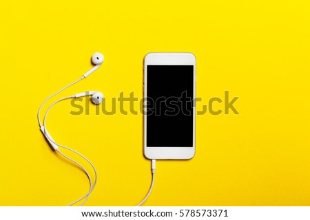 Close-up of smart phone with headphones on a yellow background. (Top view). Listen to music.

