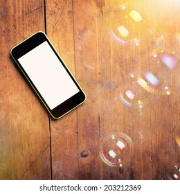 Closeup of smart phone with isolated white screen and bubbles on wooden surface. Square image with instant filter. Modern warm colored photo. Contemporary concept. Mock-up. Copy space available.