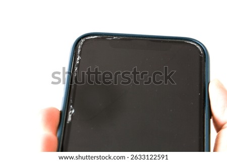 Close-up of a smartphone with a cracked screen protector, held in hand. The damage is visible at the top edge, showing chipped and fractured glass