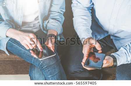 Close-up of smartphones in hands of young man and woman,dressed in jeans and shirts.Couple using digital gadgets for online shopping, chatting, blogging, surfing internet,sms. Instagram filter.