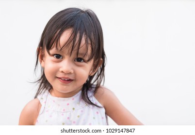 Closeup Smiley Face Of Adorable Asian Little Girl In The Background Of White Wall.