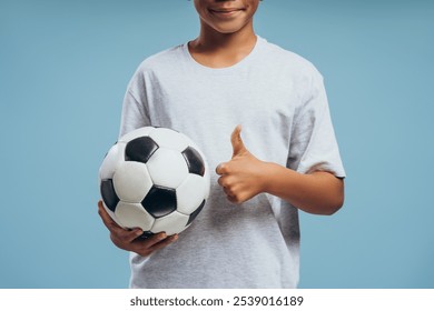 Closeup, smiling African American boy, teenager holding soccer ball showing thumb up, gesturing isolated on blue background. Playing soccer concept - Powered by Shutterstock