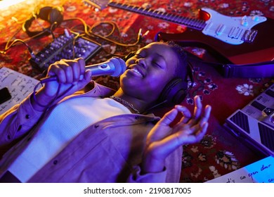 Closeup Of Smiling Black Woman Holding Microphone And Singing Lying On Carpet In Purple Neon Light