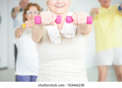 Close-up of smiling elderly person working out with pink dumbbells
