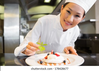 Closeup of a smiling female chef garnishing food in the kitchen