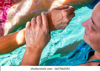 Close-up of smiling female massage therapist holding senior woman's hand during water massage in swimming pool during spa session on sunny day