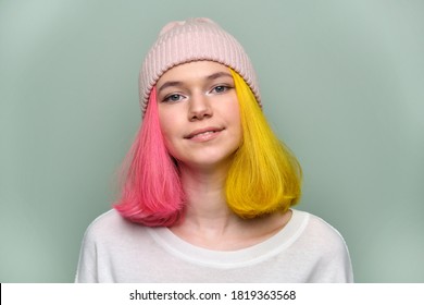 Close-up smiling female positive face, portrait of trendy teenager girl with colored dyed hair, young hipster in knitted hat on green pastel background. Adolescence, fashion, hair, beauty, lifestyle