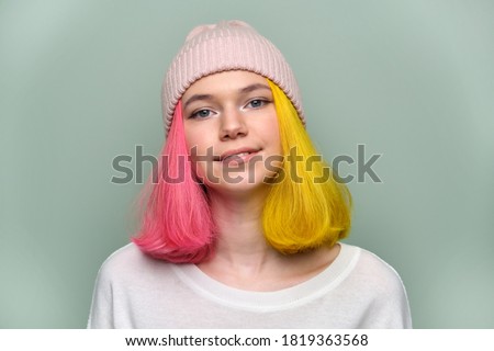Close-up smiling female positive face, portrait of trendy teenager girl with colored dyed hair, young hipster in knitted hat on green pastel background. Adolescence, fashion, hair, beauty, lifestyle