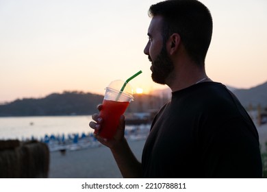 Close-up Of A Smiling, Happy Young Man Holding A Slushie With A Straw At Sunset