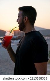 Close-up Of A Smiling, Happy Young Man Holding A Slushie With A Straw At Sunset