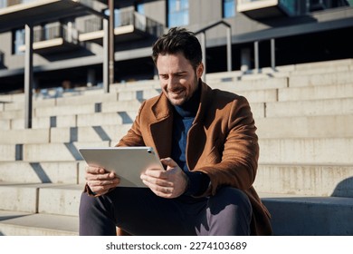 Closeup of smiling man wearing coat relaxing with digital tablet on stairs in city - Powered by Shutterstock