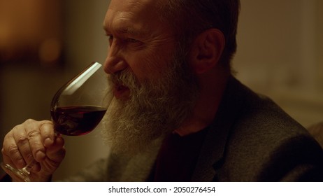 Closeup Smiling Senior Man Drinking Red Wine Glass Indoors. Handsome Elderly Gentleman Tasting Alcohol Restaurant. Old Man Face Enjoy Drink, Grandfather Enjoy Celebrating Birthday Anniversary Home