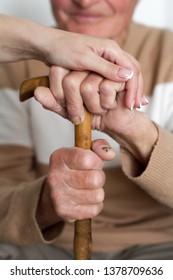 Closeup of smiling senior mans hands and young girl caregiver holding hands on walking stick, concept of care for young people about the elderly