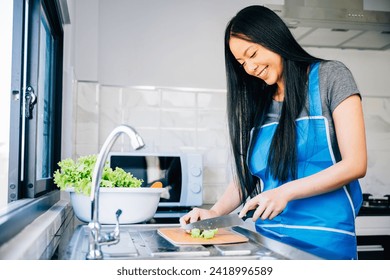 Close-up of a smiling woman in an apron cutting vegetables for a healthy salad. Emphasizing the housewife's preparation of a nutritious meal for dinner.
