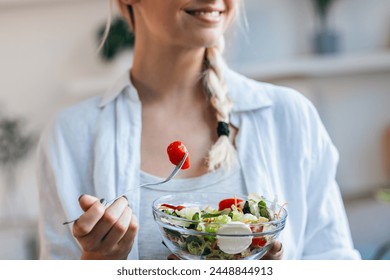 Closeup of smiling woman eating healthy salad while sitting on the kitchen at home. - Powered by Shutterstock