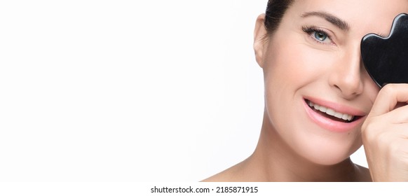 Closeup Of Smiling Woman Face With Luminous Healthy Skin Displaying A Massage Gua Sha Tool. Isolated On White With Copyspace