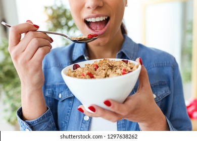 Close-up of smiling young woman eating breakfast cereals of bowl at home.